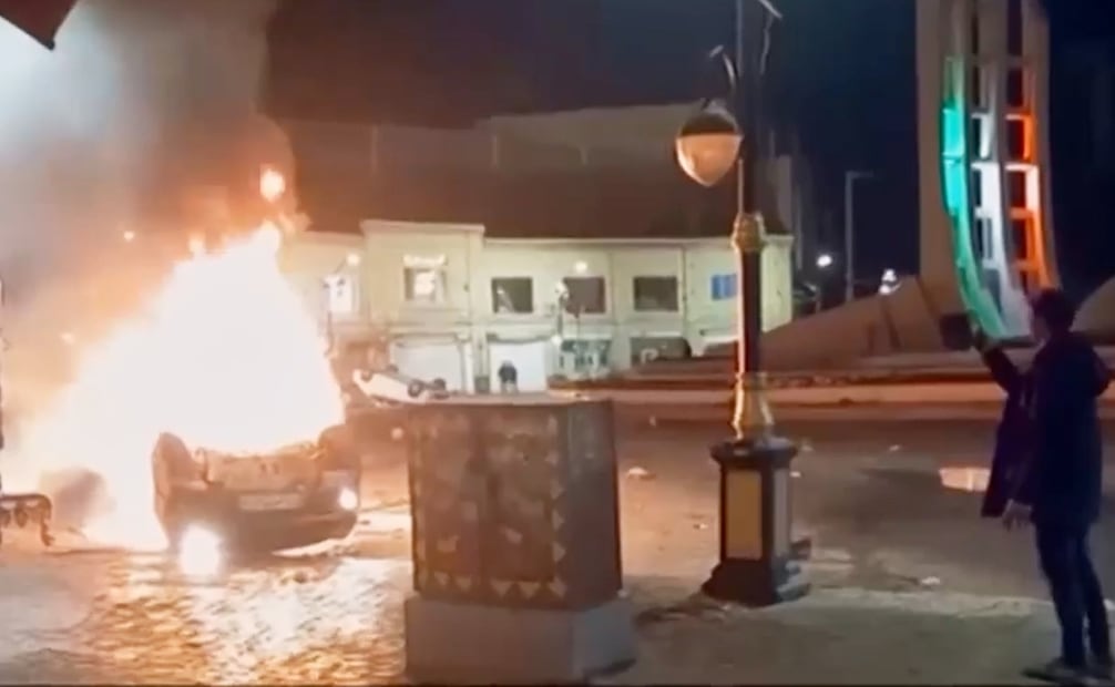 Esta captura de pantalla de un video publicado el viernes 9 de enero de 2026 por la televisión estatal iraní muestra a un hombre sosteniendo un dispositivo para documentar vehículos en llamas durante una noche de protestas masivas en Zanjan, Irán. Foto: AP