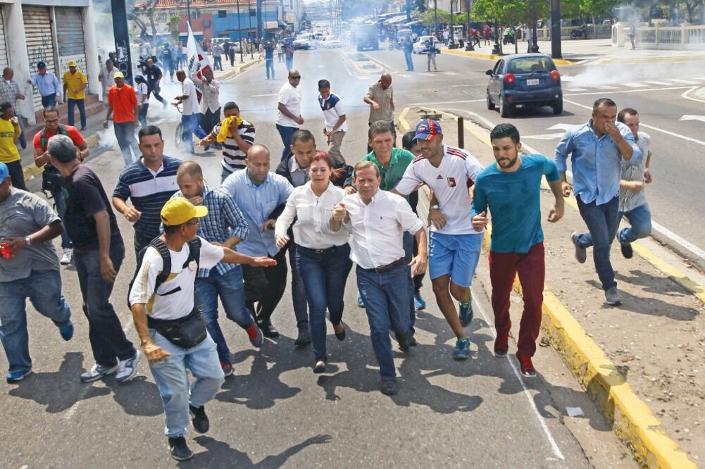 Juan Pablo Guanipa, gobernador electo de Zulia, y partidarios de la oposición huyen luego de que la policía dispersara la manifestación con gas lacrimógeno, en Maracaibo. (ISAAC URRUTIA. REUTERS)