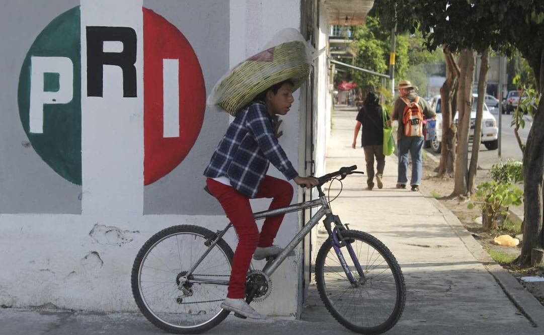 Un joven panadero espera iniciar la venta de su producto en una esquina del poblado de Alpuyeca. Al fondo, un mural que contiene el logo del PRI. Foto: Cuartoscuro