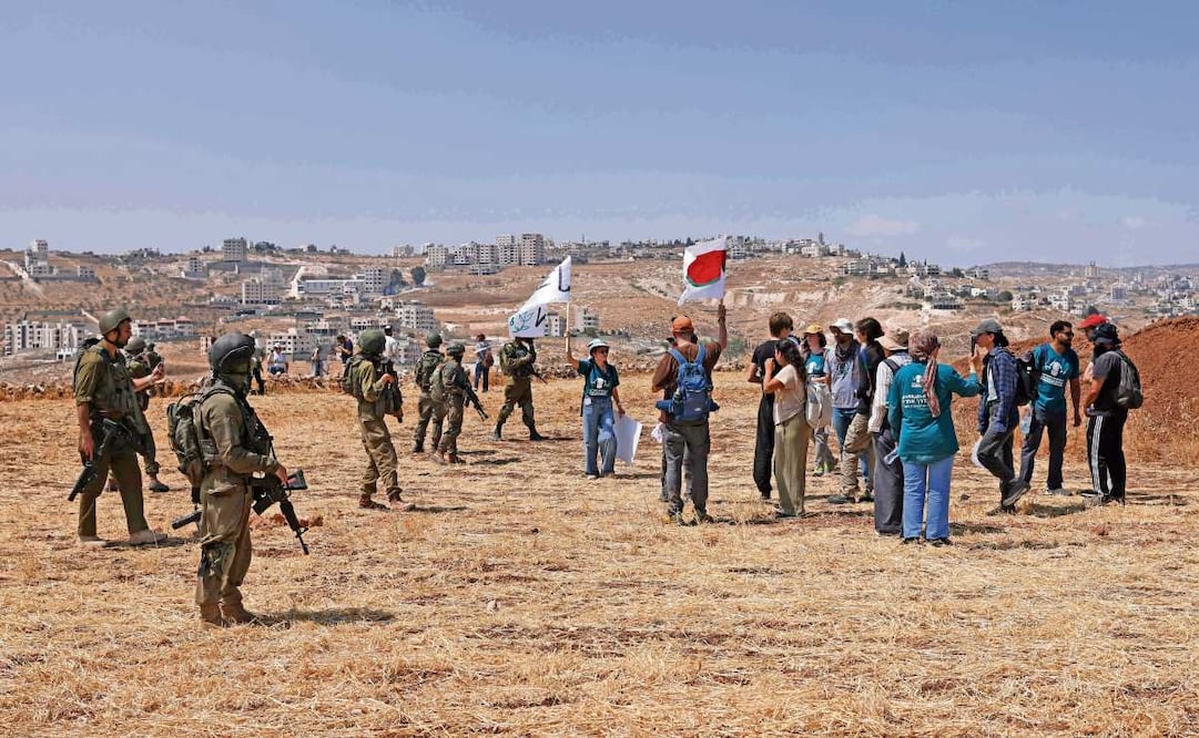 Activistas, junto a soldados israelíes mientras acompañan a propietarios palestinos a sus tierras —en riesgo de ser confiscadas por colonos israelíes—, en Cisjordania ocupada. Foto: AHMAD GHARABLI/AFP