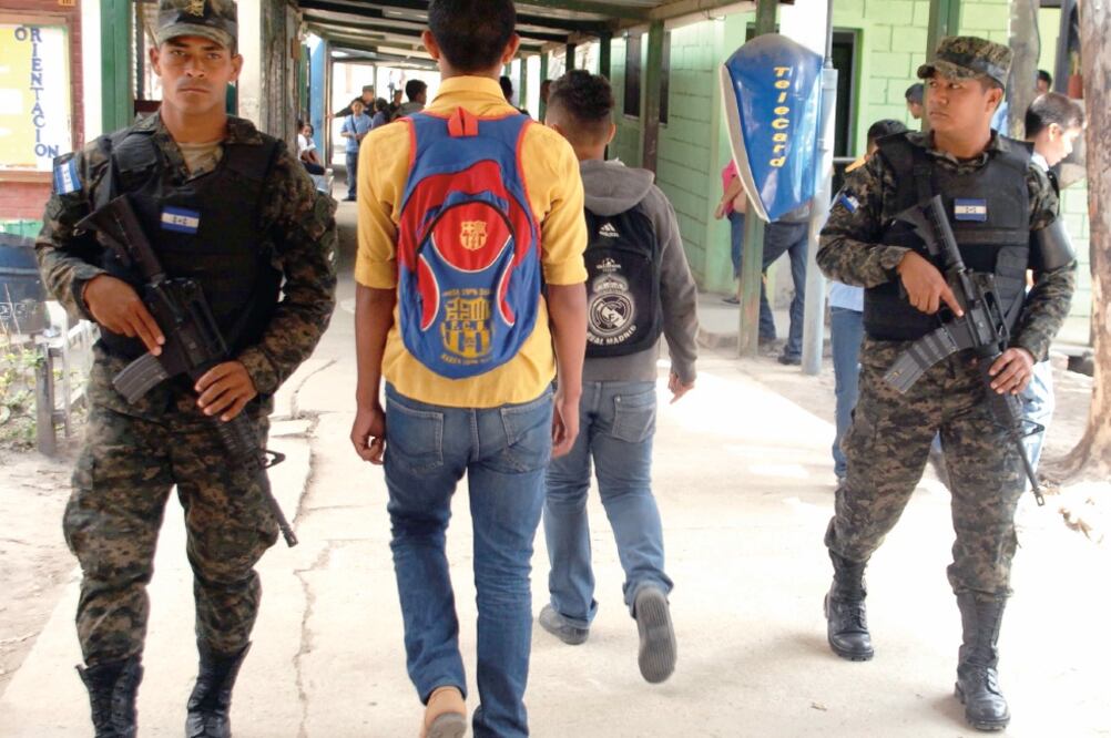 Un estudiante hondureño pasa entre dos soldados de Honduras en un pasillo de uno de los colegios de Tegucigalpa que fue militarizado para enfrentar el asedio de las maras o pandillas juveniles (CORTESÍA LA TRIBUNA)
