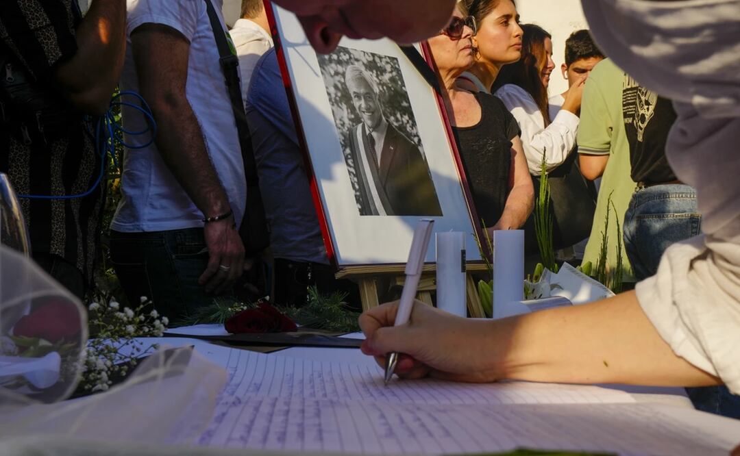 Un retrato del fallecido expresidente chileno Sebastián Piñera en el punto de homenaje colocado en la sede del partido Renovación Nacional, mientras una mujer firma en el libro de condolencias, en Santiago, Chile. Foto: AP