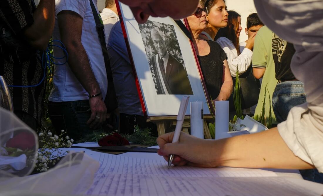 Un retrato del fallecido expresidente chileno Sebastián Piñera en el punto de homenaje colocado en la sede del partido Renovación Nacional, mientras una mujer firma en el libro de condolencias, en Santiago, Chile. Foto: AP