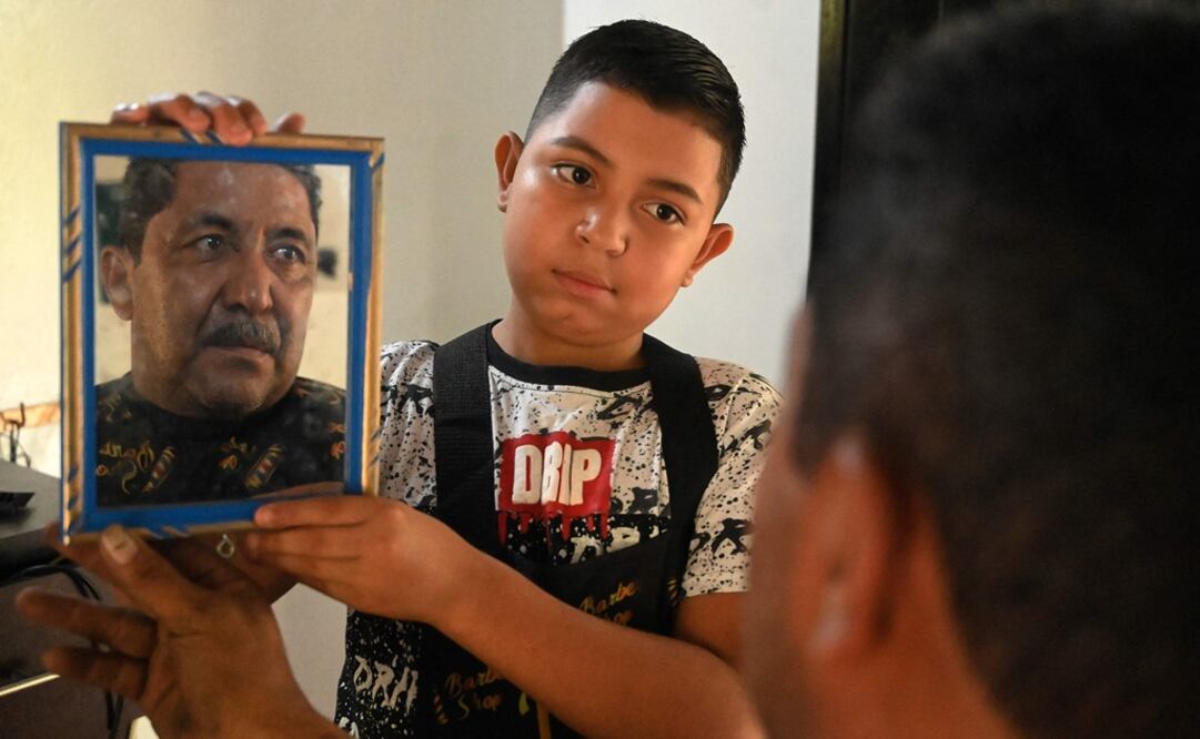 Eduardo Espinal, un niño de 12 años, muestra a un cliente su corte de cabello en su barbería en Comayagua, Honduras. Foto: AFP