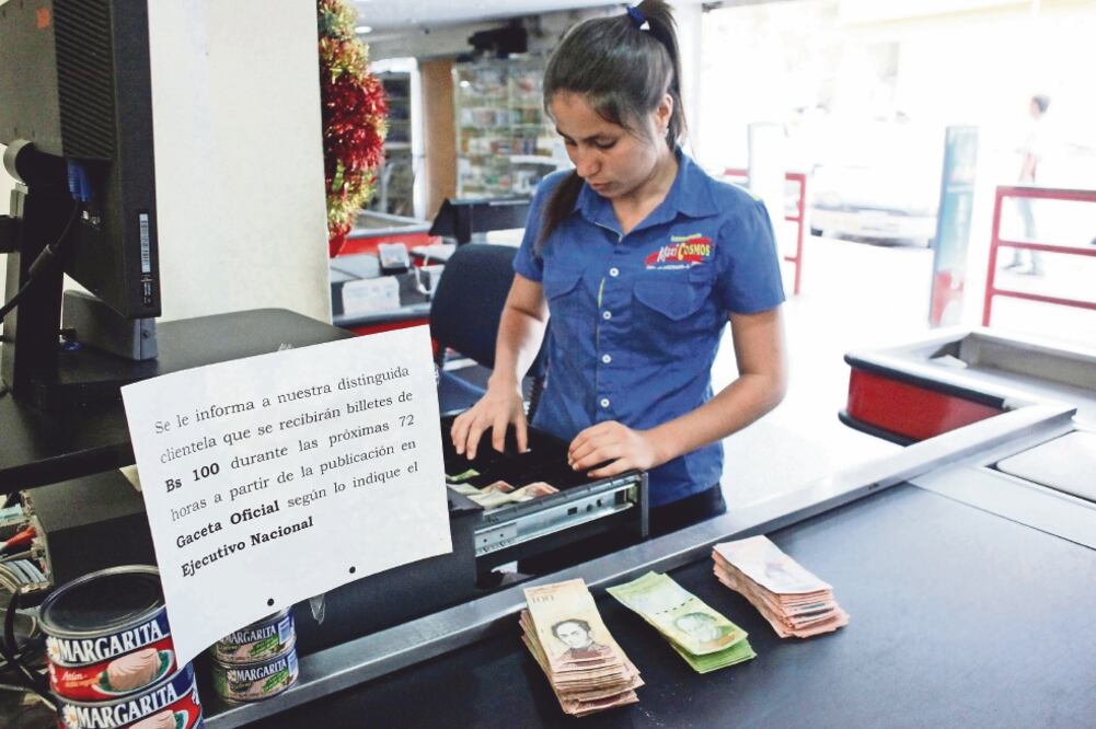 Una cajera en un supermercado en San Cristobal junto a un mensaje en el que se avisa que sólo recibirán billetes de 100 bolívares hasta mañana (CARLOS EDUARDO RAMÍREZ. REUTERS)