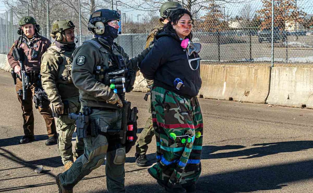 Las fuerzas del orden vigilan a los manifestantes que protestan frente al Edificio Federal Bishop Henry Whipple durante una protesta contra las operaciones del Servicio de Inmigración y Control de Aduanas (ICE) de Estados Unidos, en Minneapolis, Minnesota, el 1 de marzo de 2026. La manifestación se organizó en relación con un campamento de oración establecido al otro lado de la calle, en el sitio sagrado de Mni Owe Sni (Coldwater Spring), donde organizadores indígenas se han reunido en las últimas semanas para orar por las familias afectadas por las medidas migratorias y pedir la "Fuera ICE" y la "Devolución de Tierras". Los líderes indígenas afirman que la aplicación de la ley migratoria y la detención reflejan patrones históricos de desplazamiento y encarcelamiento experimentados por las comunidades nativas. El campamento en Mni Owe Sni, considerado un sitio sagrado de los Dakota, se estableció para celebrar ceremonias, oraciones y solidaridad con las familias inmigrantes. Foto: AFP