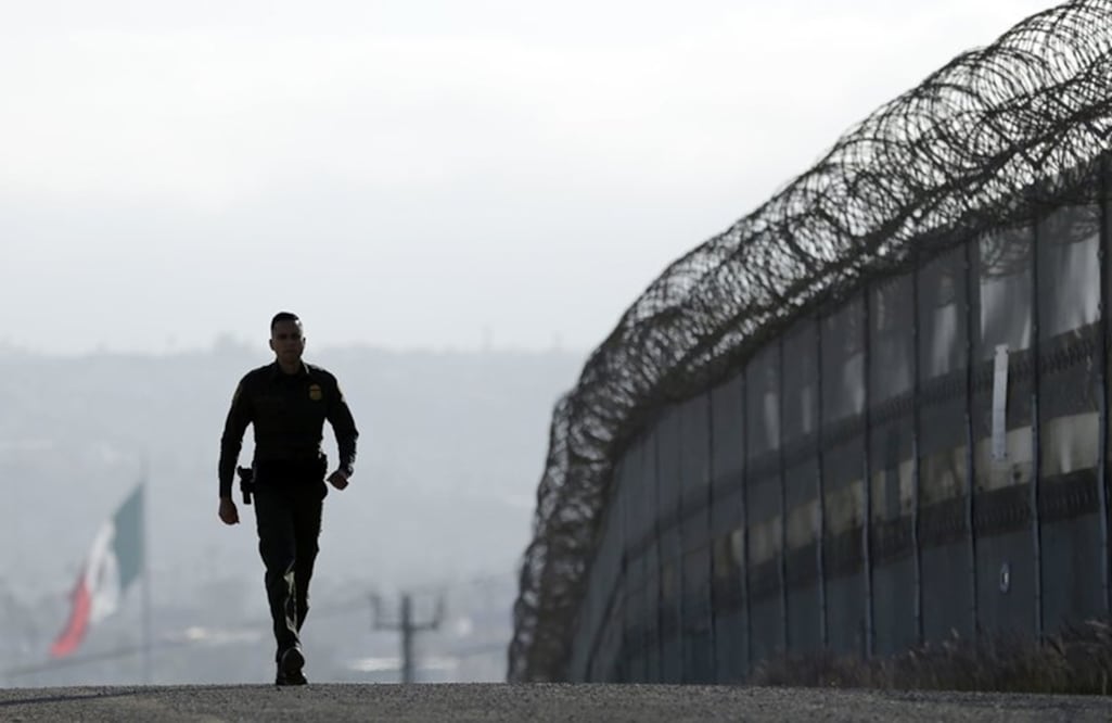 In this June 22, 2016 file photo, Border Patrol agent Eduardo Olmos walks near the secondary fence separating Tijuana, Mexico, background, and San Diego in San Diego. (AP Photo/Gregory Bull, file)