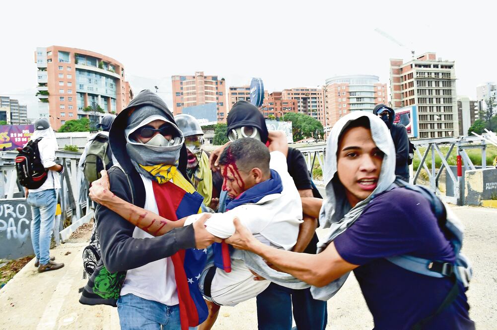 Activistas de la oposición venezolana se llevan a un compañero herido durante los enfrentamientos de ayer con la policía antimotines, en una marcha en Caracas (RONALDO SCHEMIDT. AFP)