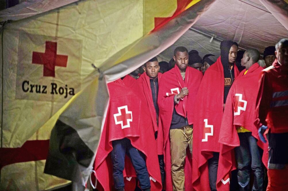 Un grupo de migrantes africanos se resguardan en una carpa de la Cruz Roja después de su arribo a la costa de la ciudad de Málaga, España, después de que un bote inflable con 150 personas fuera rescatado por las autoridades (JORGE GUERRERO. AFP)