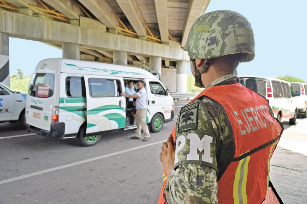 Un elemento del Instituto Nacional de Migración verifica la identificación de un pasajero mientras que un agente de la Policía Militar vigila un puesto de control a las afueras de Tapachula, en el estado de Chiapas. Foto: JOSÉ TORRES. REUTERS