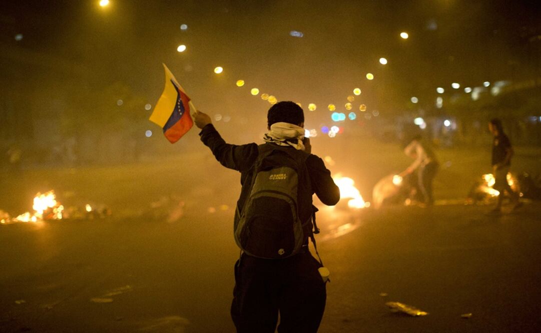 An anti-government demonstrator holds a representation of Venezuela's national flag in front of a burning barricade – Photo: Rodrigo Abd/AP	