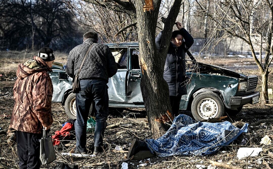 Personas esperan junto al cuerpo de un pariente tendido en el suelo después de los bombardeos en la ciudad de Chuguiv, en el este de Ucrania.   Foto: AFP