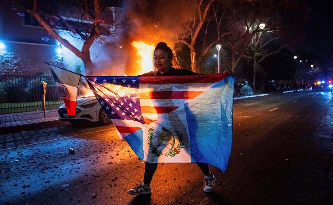 Una persona con una combinación de banderas camina frente a un auto incendiado durante las protestas por las redadas del gobierno de Trump en Los Ángeles, el lunes 9 de junio de 2025. Foto: AP