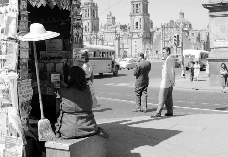 Una escena cotidiana en la esquina de Pino Suárez y Corregidora a finales de los años cincuenta. En el fondo se aprecian el Zócalo y la Catedral Metropolitana, y en el puesto de periódicos aparecen algunas revistas de la época, como "Mecánica Popular", "Confidencias", "Box y Lucha" o "Life". 