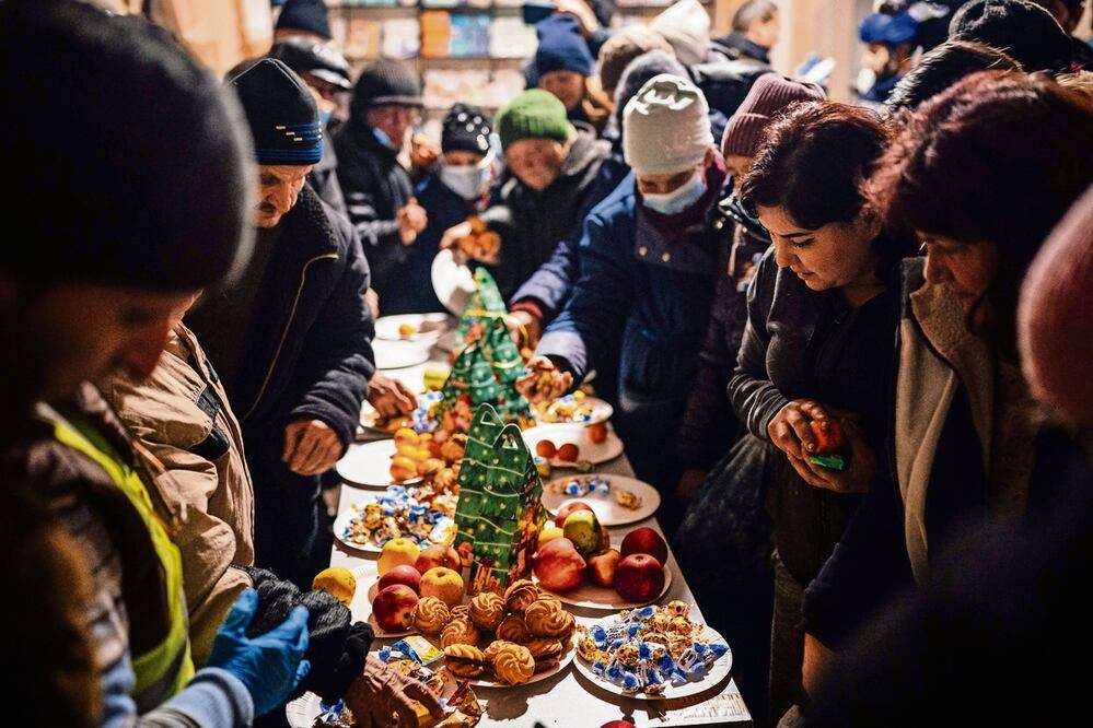 Los residentes locales se reúnen alrededor de una mesa navideña para servirse pequeños pasteles y frutas, en un centro de ayuda humanitaria en Bakhmut, región de Donetsk, el 6 de enero de 2023. Foto: AFP