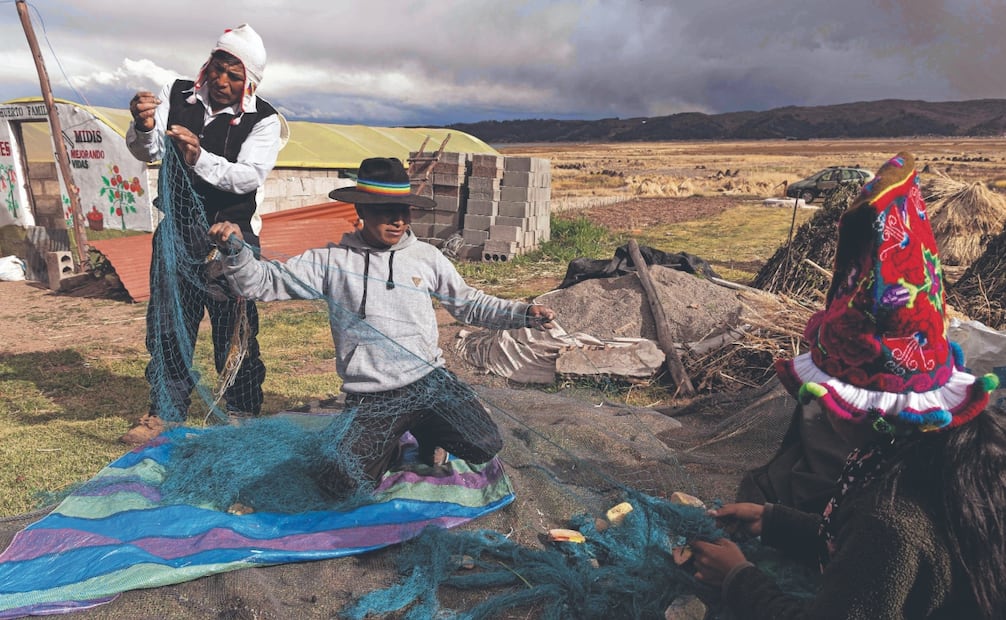 Efraín Vilca (izquierda) y su familia reparan una red de pesca en la comunidad de Acora, a orillas del lago Titicaca, región de Puno, Perú. Foto: AFP