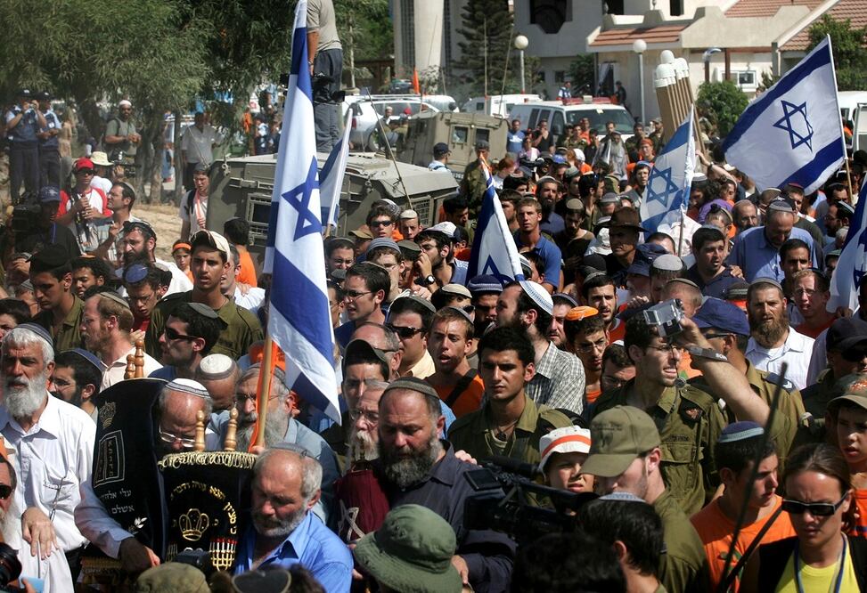 Colonos israelíes marchan con banderas, al salir del asentamiento judío de Netzarim, en la Franja de Gaza. FOTO: AP