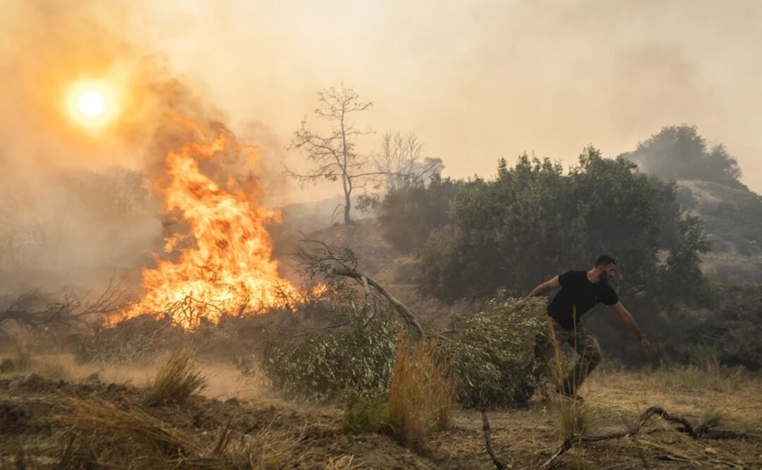 Ilias Kyriakou, de 25 años, arrastra una rama de olivo mientras un incendio quema parte de la localidad de Gennadi, en la isla de Rodas, en el sureste de Grecia, el 25 de julio de 2023. Foto: AP