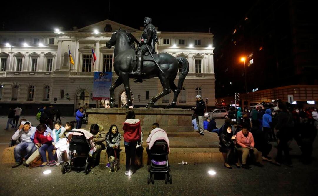 Ciudadanos permanecen sentados junto a una estatua ecuestre en la plaza principal de Santiago luego del terremoto. FOTO: AP