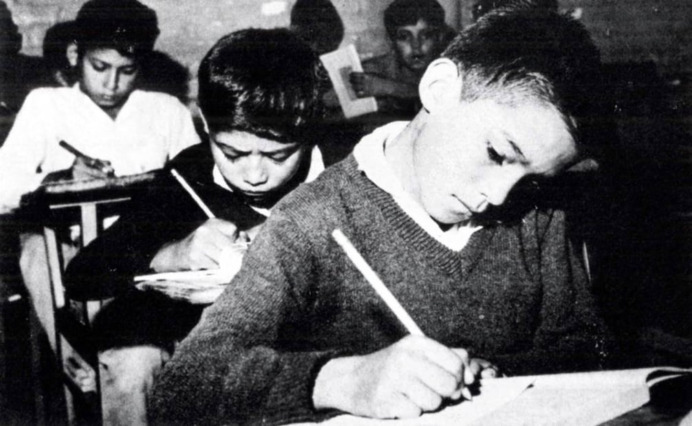 Típico salón de clases de mediados de los años setenta. Los niños apuntan todo lo que les va dictando el maestro;  muchas materias eran impartidas de esta manera, ya que al escribir se reforzaba lo que venía en el libro de texto, más lo que explicaba el maestro. La materia de historia era en gran parte memorizar pasajes relevantes del pasado y su peso en la transformación de los hechos. Colección Villasana.