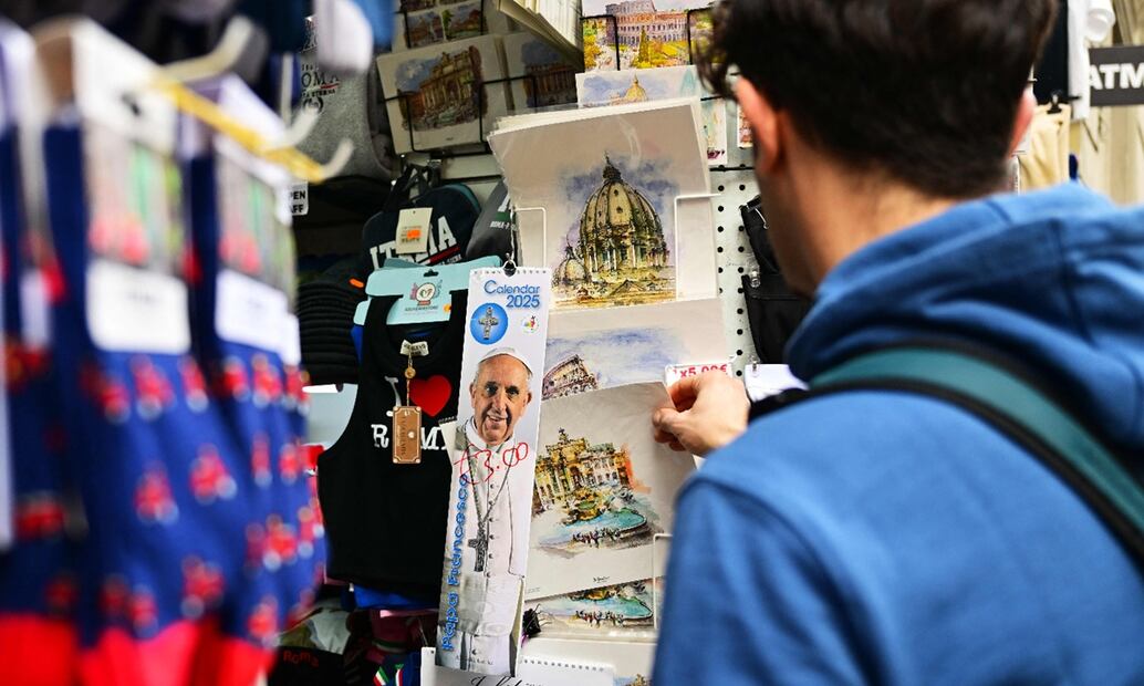 Un turista observa recuerdos turísticos, incluyendo algunos con el retrato del papa Francisco y etiquetas de precio, en una tienda un día antes del funeral del Pontífice, en Roma, el 25 de abril de 2025. Foto: AFP