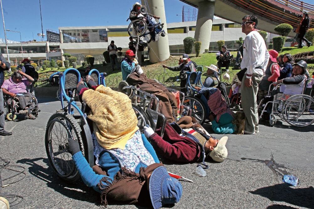 Bolivianos discapacitados bloquean una avenida mientras una mujer en silla de ruedas es suspendida en el aire, durante la protesta del martes, en La Paz (MARTÍN ALIPAZ. EFE)