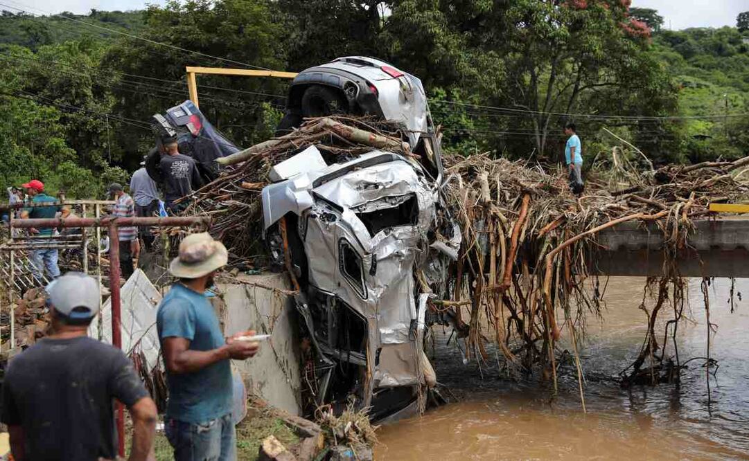 Un grupo de personas observa vehículos arrastrados por la corriente del río este viernes, al este de Tegucigalpa (Honduras). Foto: EFE