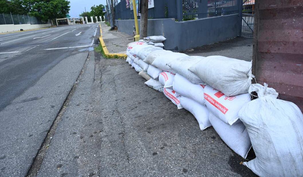 Habitantes colocan bolsas de arena como barrera en la entrada de un local como prevención para la llegada del huracán Beryl en una calle de Kingston, Jamaica. Foto: EFE