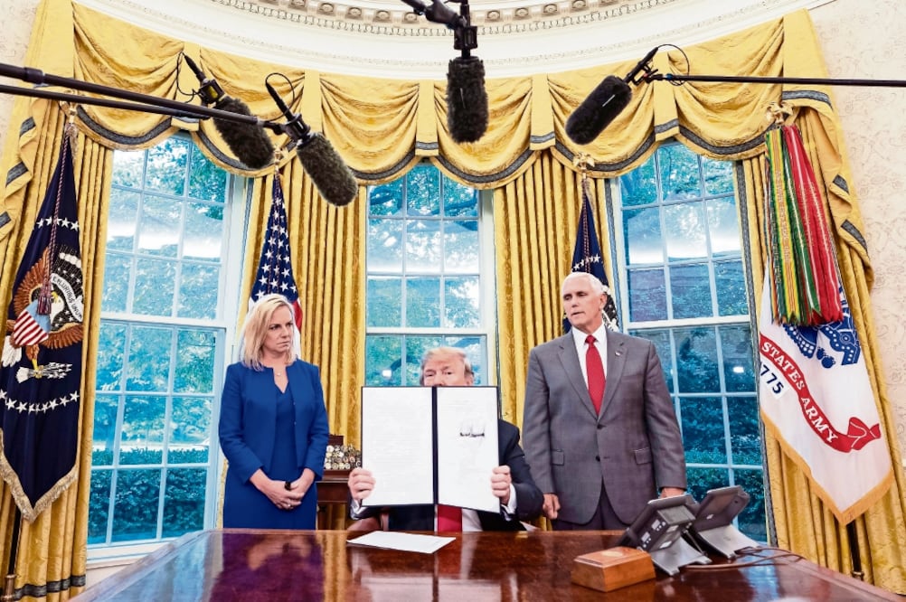 Donald Trump, flanqueado por la secretaria de Seguridad Nacional, Kirstjen Nielsen (izq.), y el vicepresidente Mike Pence (der), muestra la orden ejecutiva firmada contra la separación de niños migrantes (JIM LO SCALZO. EFE)