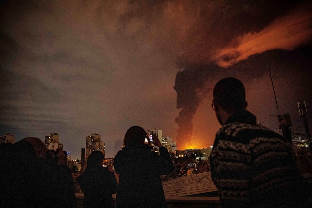 Iraníes observan el humo que sale de un depósito de petróleo atacado por Israel, en Teherán. FOTO: ALIREZA SOTAKBAR. AP