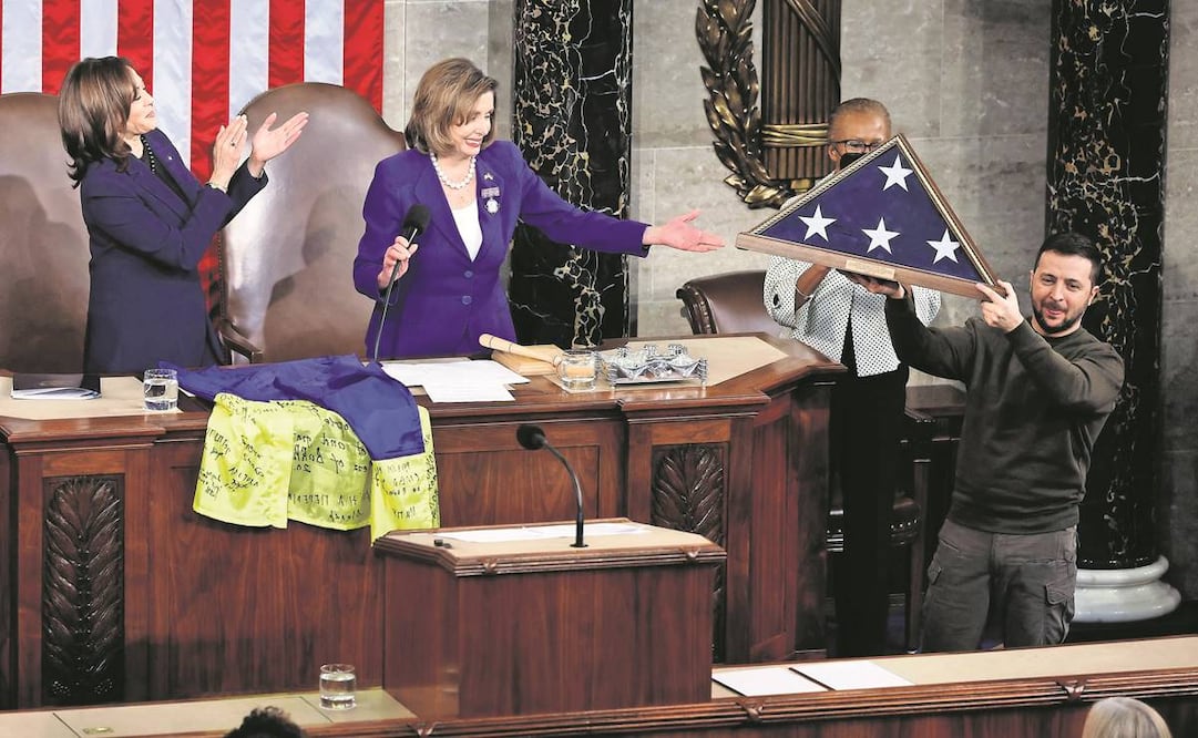 El presidente de Ucrania, Volodimir Zelensky, sostiene una bandera estadounidense. Acudió al Capitolio, donde dio un mensaje a los integrantes del Congreso, reunión a la que también asistió la vicepresidenta Kamala Harris (izq.); en el centro está la pres