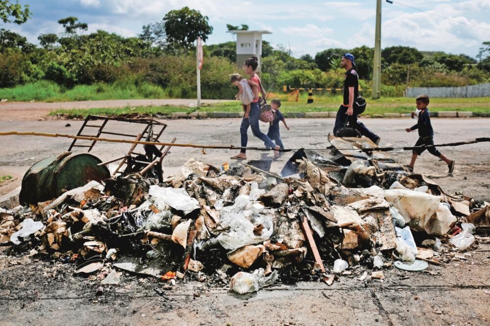Una familia de venezolanos pasa frente a los restos de un campamento de inmigrantes que fue quemado por residentes de la ciudad brasileña de Paracaima. (NACHO DOCE. REUTERS)