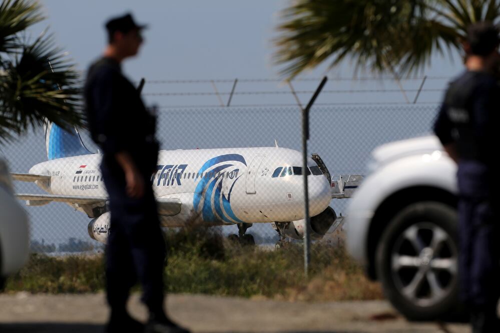 Agentes de policía hacen guardia junto a la valla de un aeropuerto con el avión secuestrado de EgyptAir en segundo plano, en el aeropuerto de Larnaca, en Chipre (AP)