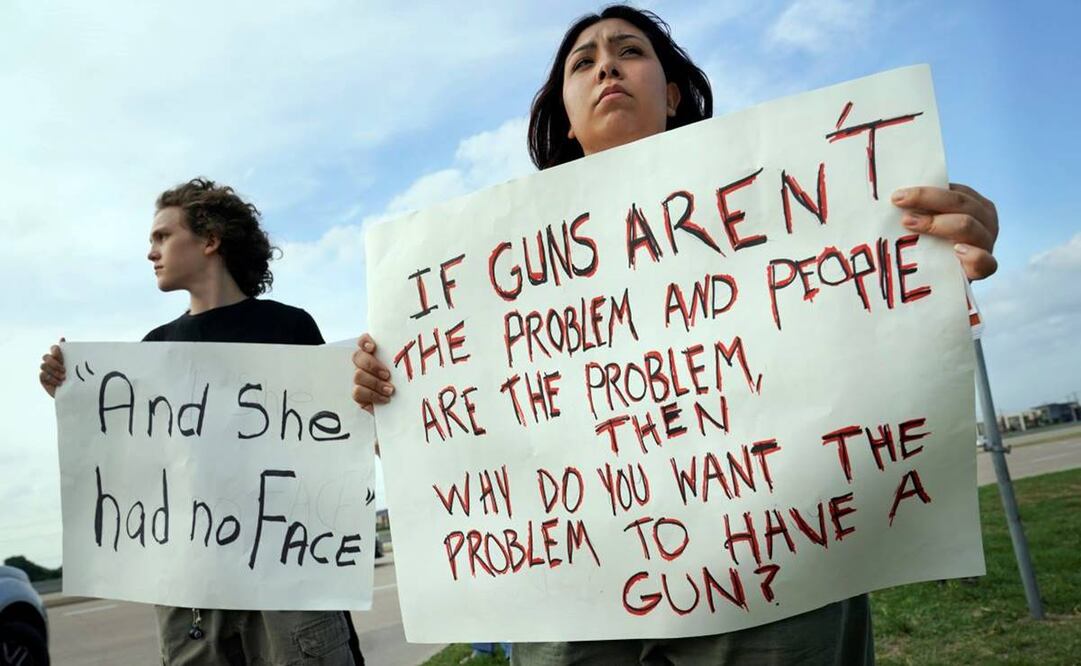 Dos jóvenes durante una protesta por el tiroteo del sábado en Allen, Texas. El letrero de él dice: "Y ella no tenía rostro", en alusión a cómo fue encontrada una de las víctimas mortales de la masacre. Foto: AP