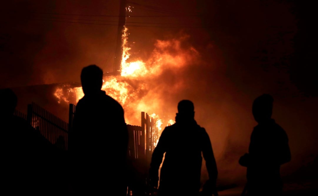 Personas observan viviendas afectadas por los incendios forestales durante la madrugada de este domingo, en Chile. (18/01/26) Foto: EFE