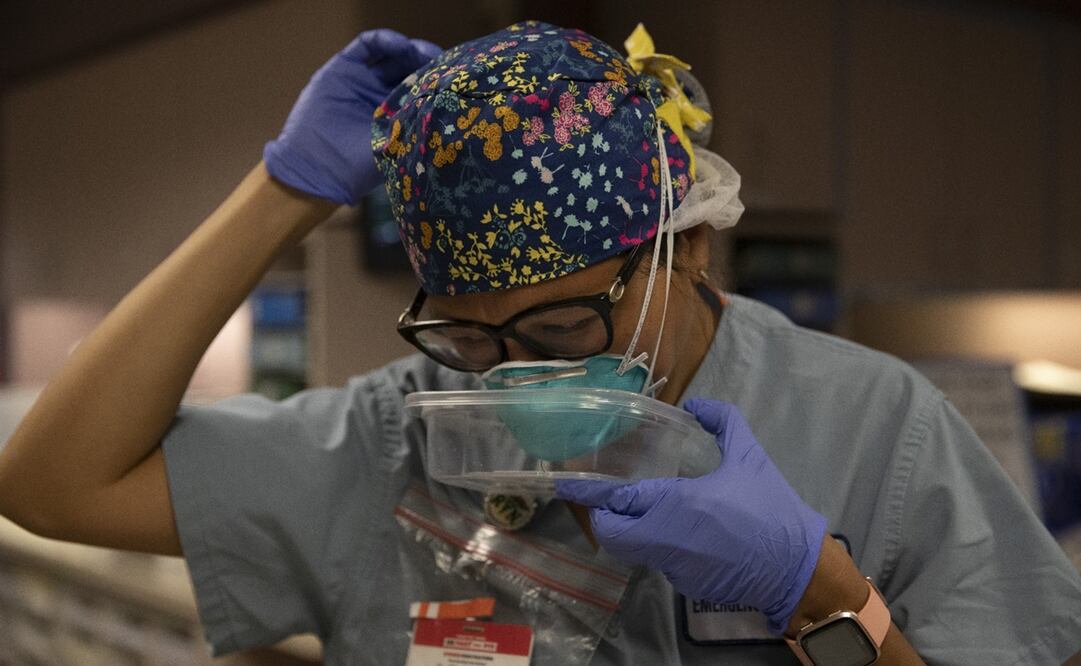 La doctora Jackie Vargas se protege el rostro con un contenedor de plástico para no estar expuesta mientras se coloca el cubrebocas. Foto: AP Photo/Jae C. Hong