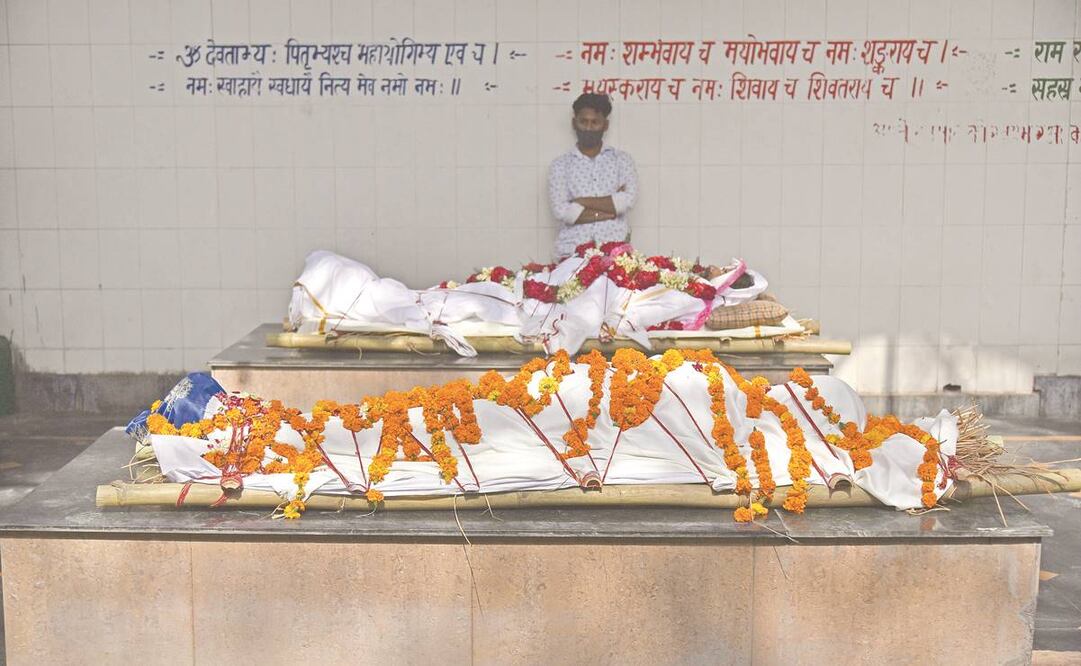Un hombre espera junto a unos cuerpos que serán incinerados en el campo de cremación en Nueva Delhi, India.