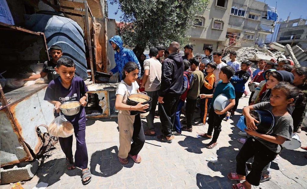 Palestinos desplazados, mientras esperan para recoger alimentos de un comedor social en el campamento de refugiados de Bureij, en el centro de la Franja de Gaza. Foto: Eyad Baba / AFP
