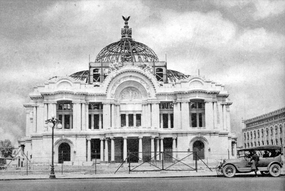 Una toma cercana a 1920 donde se aprecia la estructura inconclusa del Teatro Nacional desde la avenida Juárez. Este proyecto, realizado por Adamo Boari, inició su construcción en 1904 y se detuvo con la Revolución; más tarde fue retomado por Federico Mariscal, y para 1934 fue inaugurado como Palacio de Bellas Artes. Imagen: "The wind that swept Mexico"