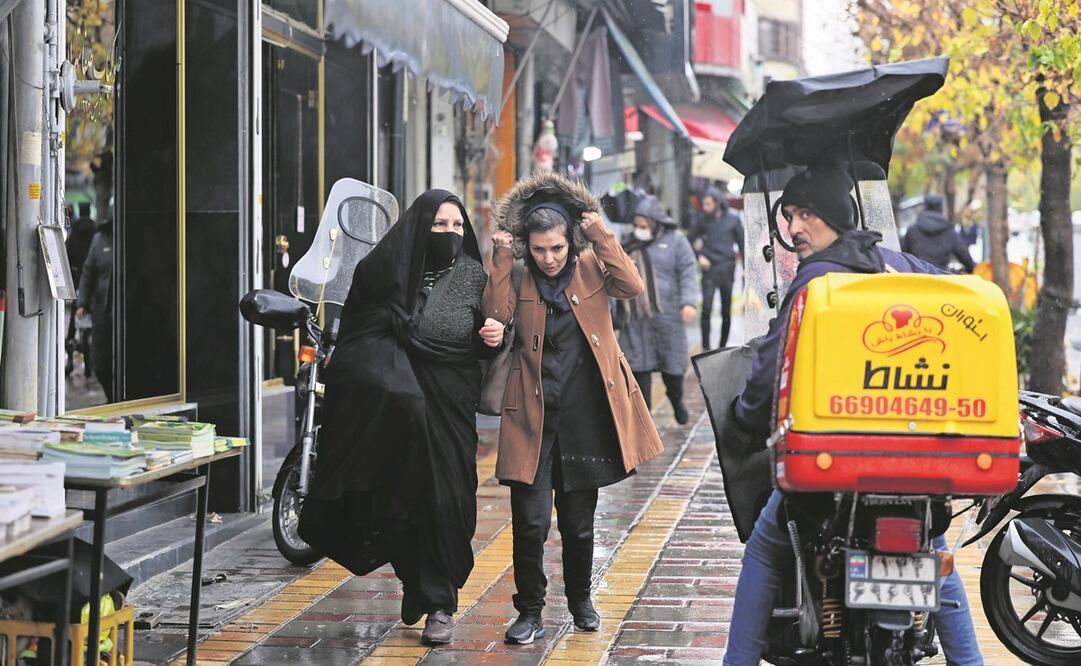 Iraníes pasan junto a algunas tiendas cerradas por la huelga convocada por manifestantes, en Teherán. Foto: EFE