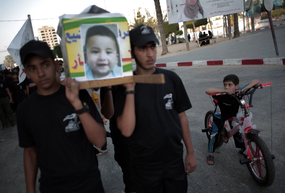 Jóvenes palestinos cargan un "ataúd" con la foto del bebé palestino y la leyenda "Ustedes lo quemaron vivo y me vengaré" (AP)