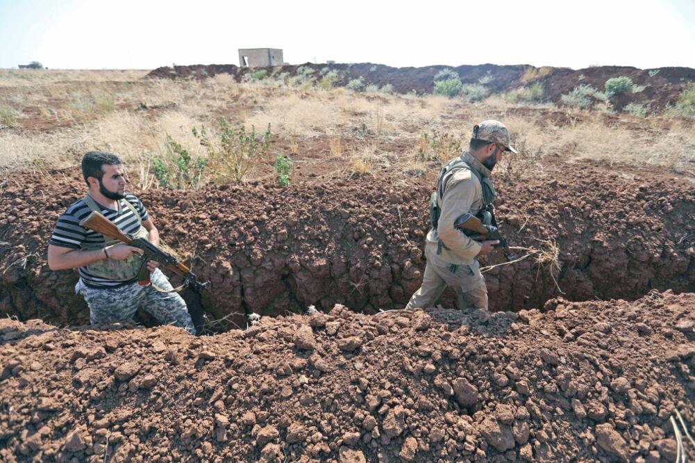 Combatientes rebeldes sirios caminan en una trinchera recién excavada en la aldea de al-Zakat, en la zona rural del norte de la provincia de Hama. (OMAR HAJ KADOUR. AFP)