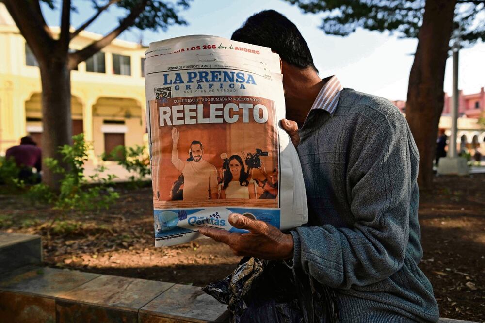 Un salvadoreño, con la portada de un periódico que dice “Reelecto” y la imagen del mandatario Nayib Bukele, con su esposa, Gabriela Rodríguez. Foto: AFP