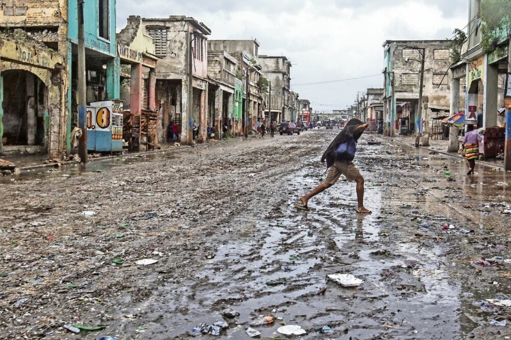 Imagen cedida por UNICEF, en la que se ve a una haitiana cruzando una calle enlodada tras el paso de Matthew, en Puerto Príncipe (XINHUA)
