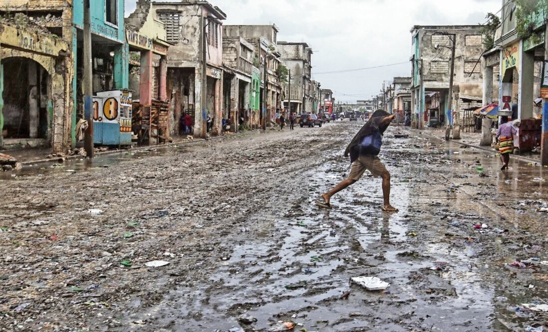 Imagen cedida por UNICEF, en la que se ve a una haitiana cruzando una calle enlodada tras el paso de Matthew, en Puerto Príncipe (XINHUA)