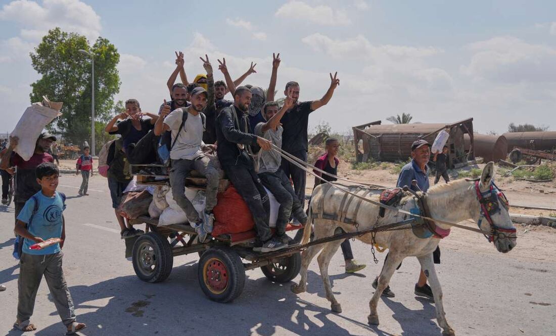 Palestinos saludan a la cámara mientras llevan paquetes de ayuda humanitaria cerca de un centro de distribución de la Fundación Humanitaria de Gaza, operado por la organización respaldada por Estados Unidos, en Netzarim, en el centro de la Franja de Gaza, el lunes 4 de agosto de 2025. Foto: AP