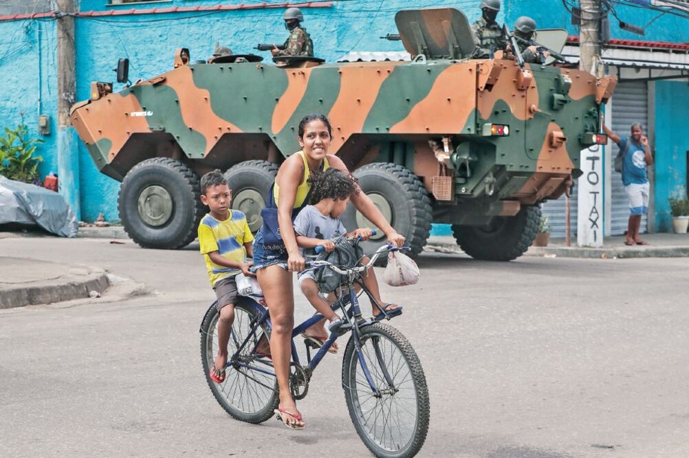 Una mujer transporta dos niños en bicicleta mientras militares de las Fuerzas Armadas brasileñas realizan un operativo, en Río de Janeiro (ANTONIO LACERDA.EFE)