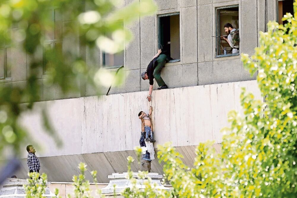 Policías iraníes sacan a un niño del edificio parlamentario atacado ayer por cuatro hombres, en Teherán. Tres de los agresores fueron abatidos y el otro se inmoló (AFP)