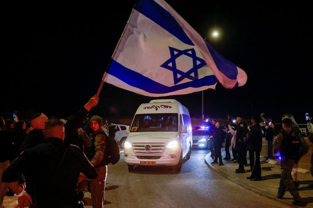 Un hombre ondea una bandera israelí mientras un vehículo que transporta a dos rehenes rusos liberados por militantes de Hamas, el 29 de noviembre de 2023 pasa por Ofakim, en el sur de Israel. Foto: AFP