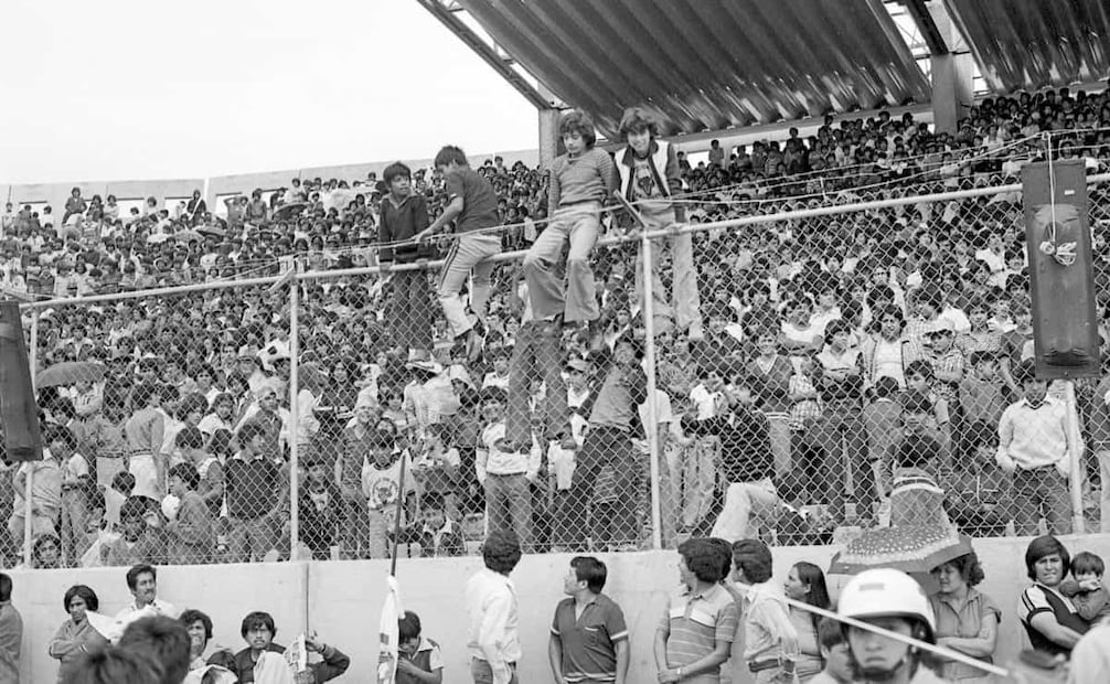 Jóvenes asistentes al partido en Neza escalaron las rejas para tener mejor visibilidad. Aunque el estadio tenía capacidad de 35 mil 500 aficionados, “acomodados con comodidad”, para la inauguración se permitió la entrada de 60 mil, apretujados en las gradas y hasta en la cancha. Foto: Archivo EL UNIVERSAL.